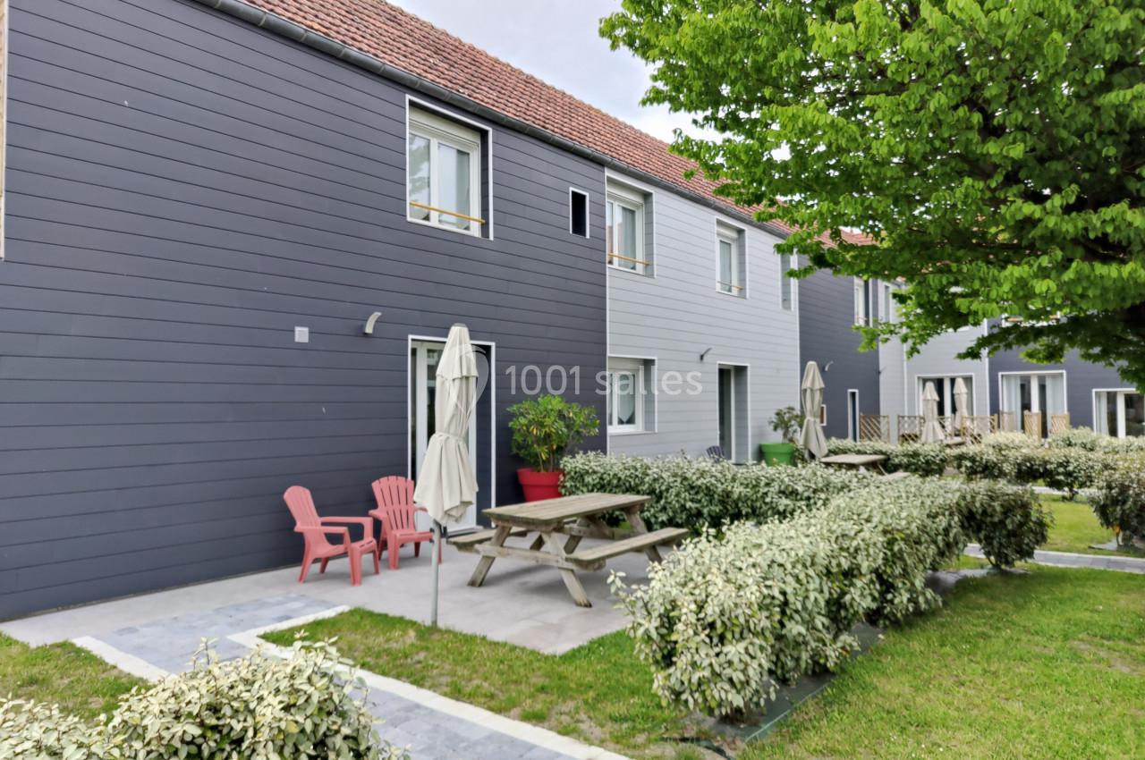 Location salle Gouville-sur-Mer (Manche) - Le Village du Phare #42 Façade de maisons modernes avec terrasse aménagée, mobilier de jardin et végétation environnante.