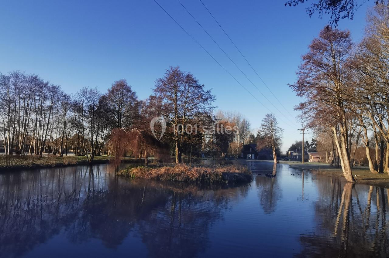 Location salle Gouville-sur-Mer (Manche) - Le Village du Phare #32 Étang calme entouré d'arbres en hiver, avec un ciel bleu dégagé et des reflets sur l'eau.