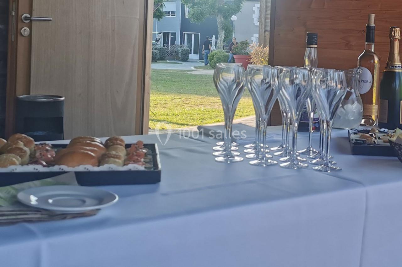 Location salle Gouville-sur-Mer (Manche) - Le Village du Phare #25 Plateau de viennoiseries et flûtes à champagne disposés sur une table blanche, avec un jardin en arrière-plan.