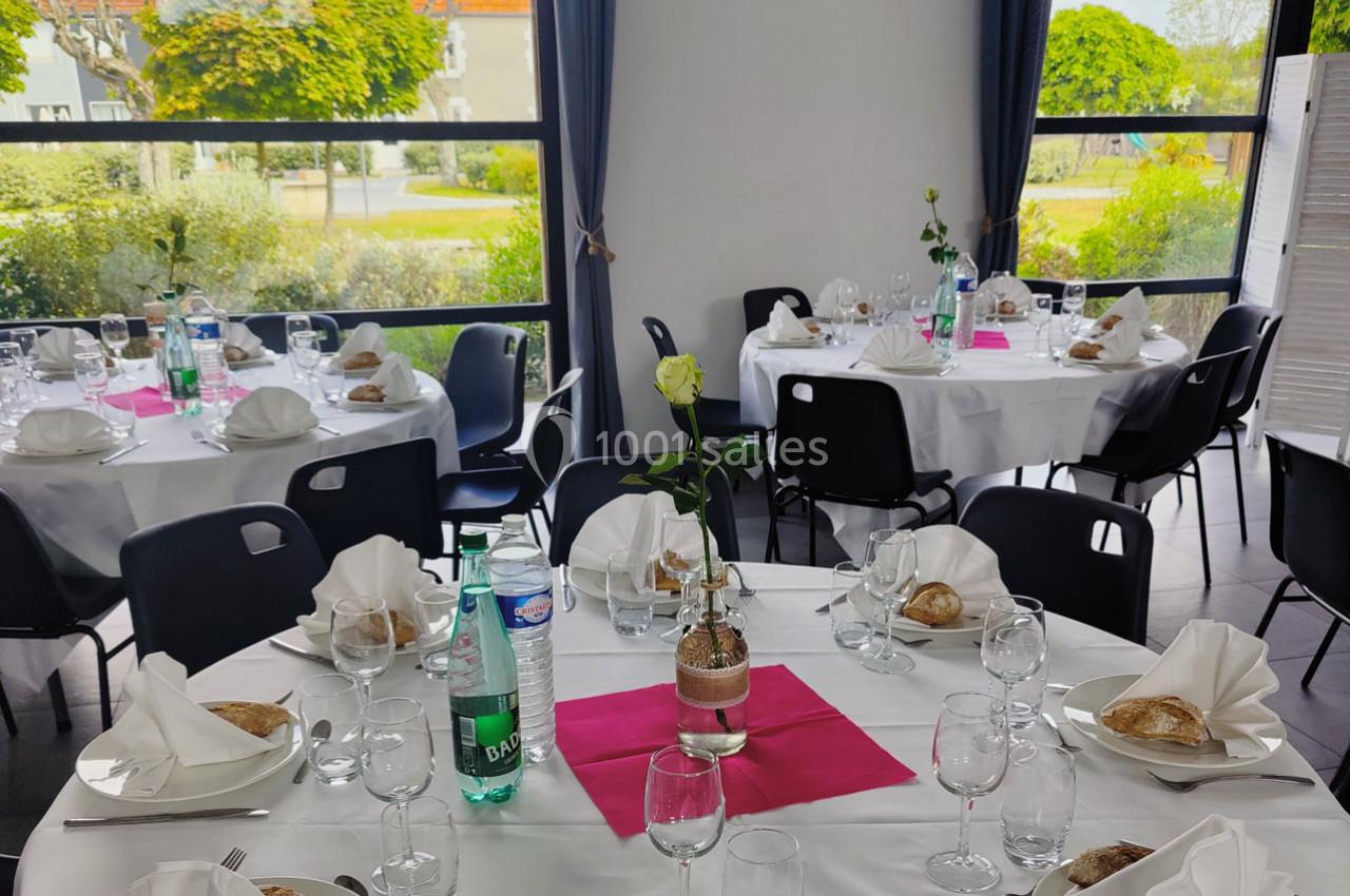 Location salle Gouville-sur-Mer (Manche) - Le Village du Phare #9 Salle de réception avec tables rondes dressées, nappes blanches, serviettes pliées, verres, et décoration florale.