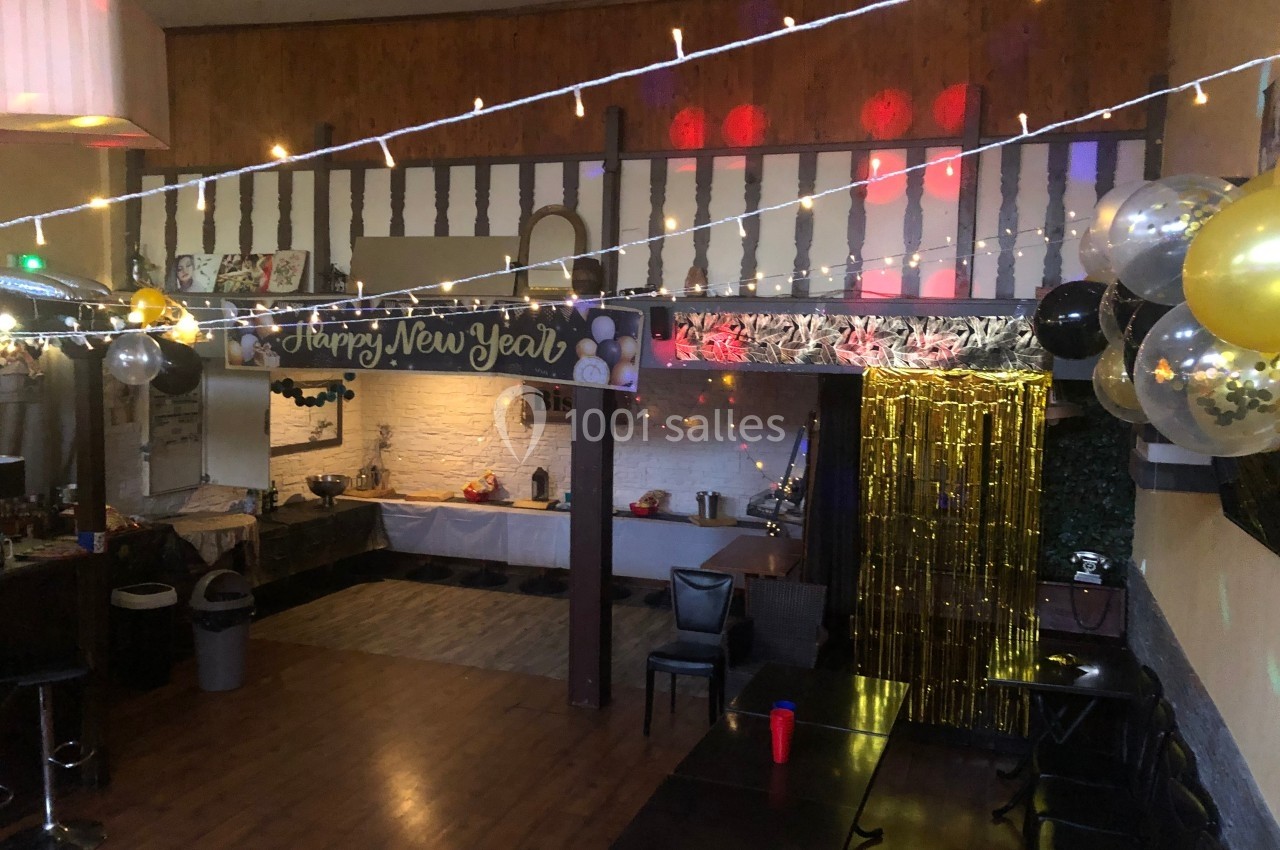 Salle décorée pour une fête avec guirlandes lumineuses, ballons dorés et noirs, et une bannière ’Happy New Year’.