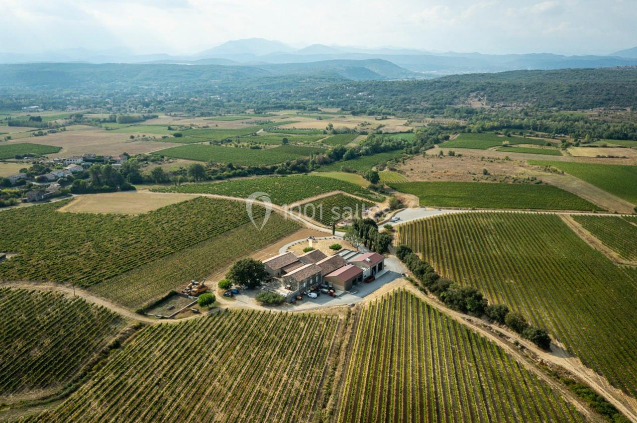 Vue aérienne d'un domaine viticole entouré de vignes et de collines verdoyantes sous un ciel clair.