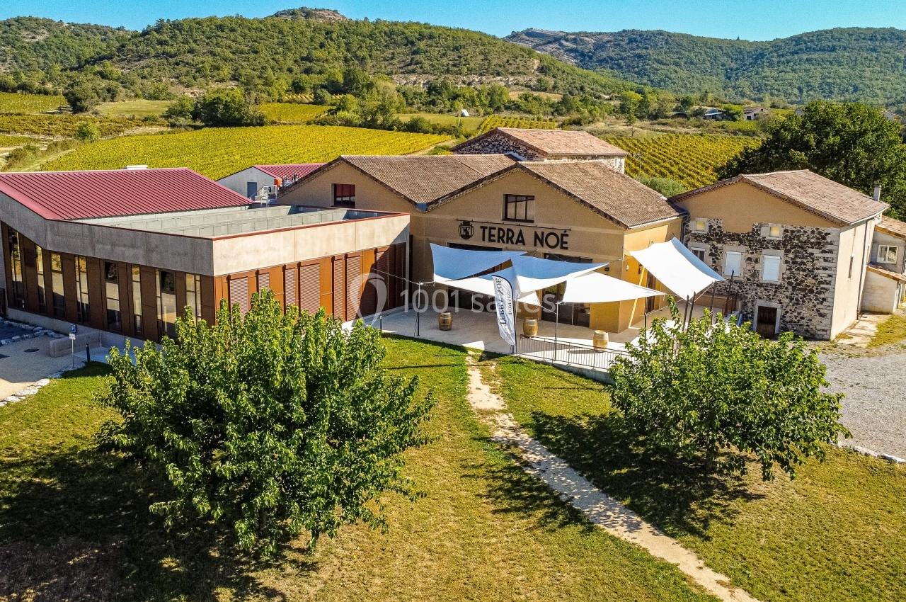 Vue aérienne d'un bâtiment viticole moderne et traditionnel entouré de vignes et de collines verdoyantes.