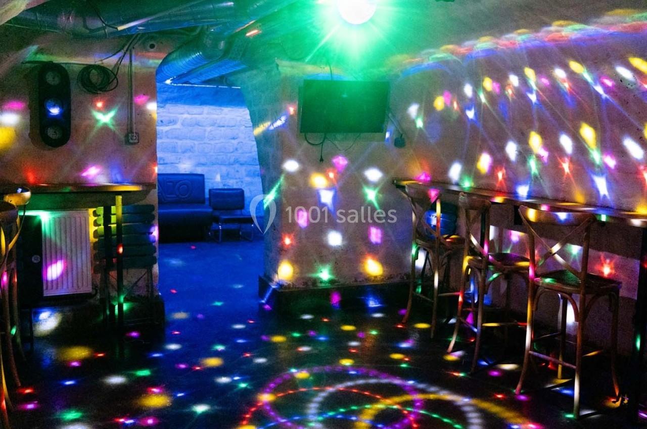Salle voûtée avec des jeux de lumières colorées projetés sur les murs et le sol, tables et chaises disposées.