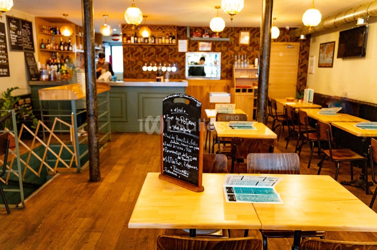 Intérieur d'un restaurant avec des tables en bois, un tableau noir affichant le menu et un bar en arrière-plan.