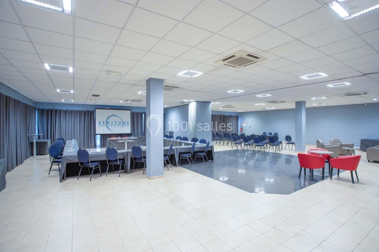 Salle de réunion spacieuse avec tables, chaises et éclairage lumineux, adaptée pour événements ou conférences.