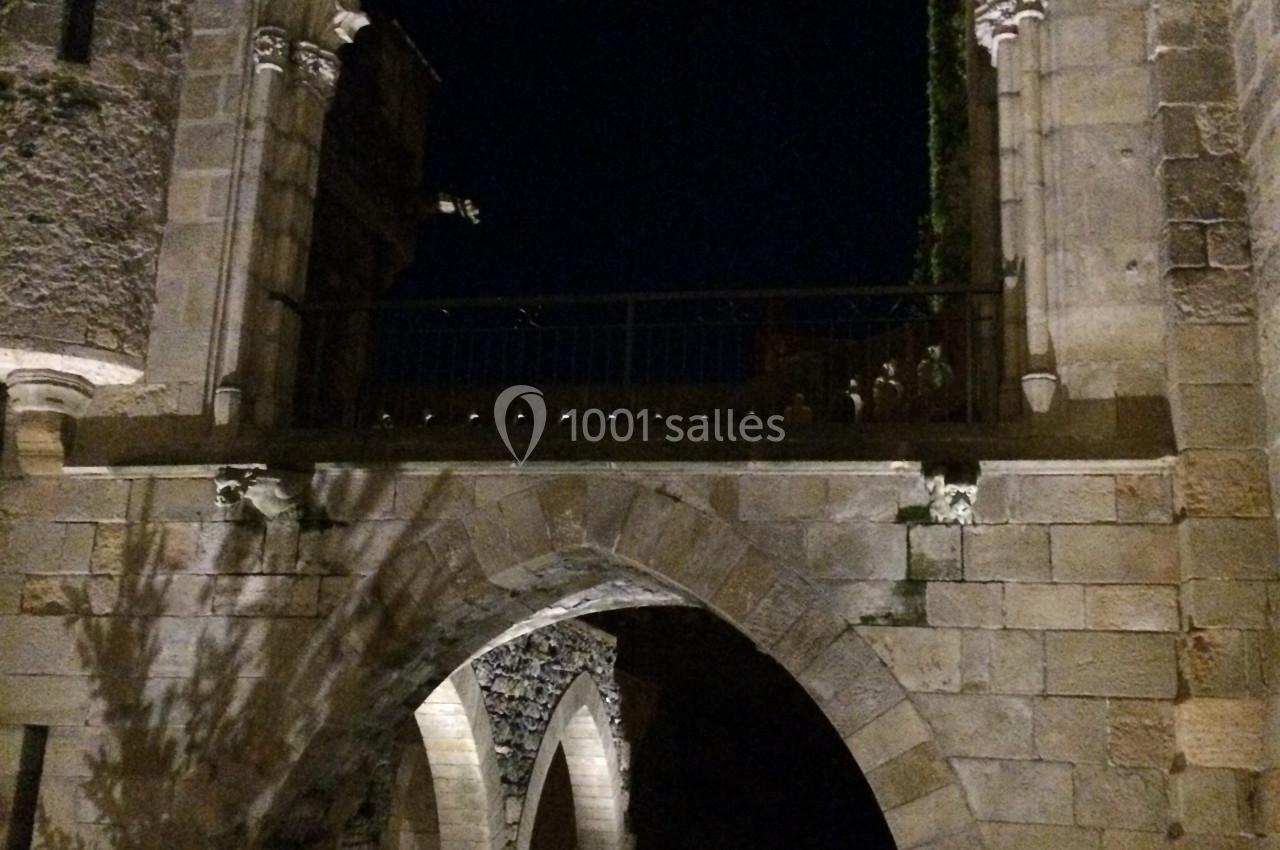 Arc gothique éclairé de nuit, encadrant un passage voûté en pierre dans un cadre architectural ancien.