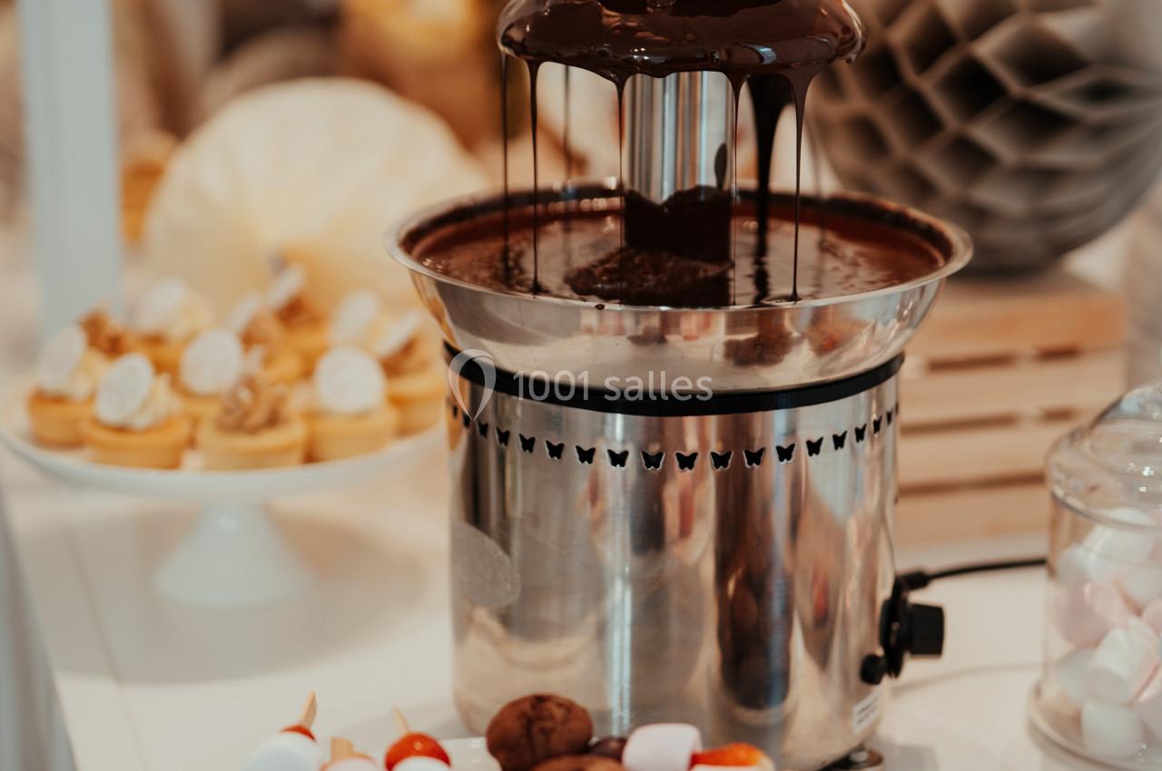 Fontaine de chocolat avec des brochettes de fruits et guimauves sur une assiette, décor de table en arrière-plan.