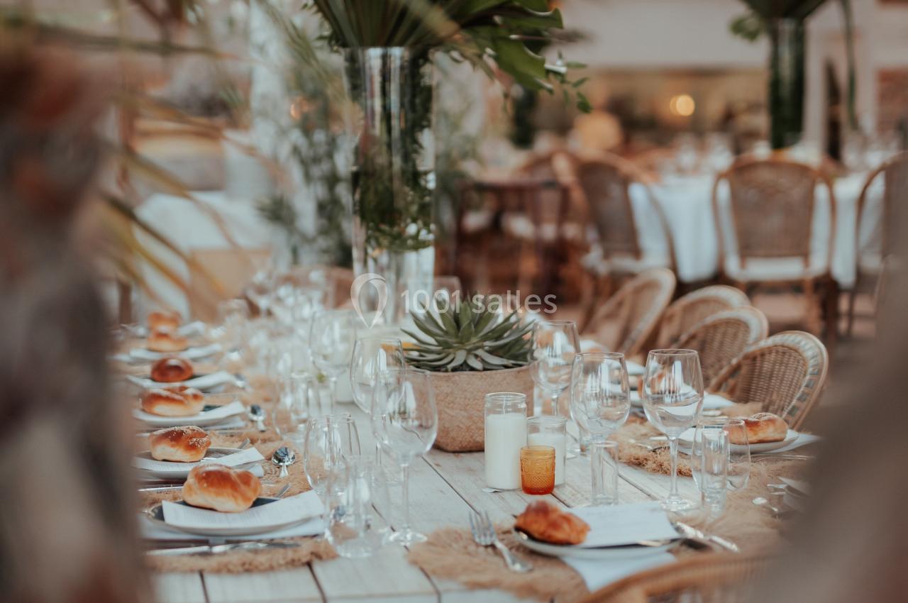 Table en bois décorée avec des plantes, des bougies et de la vaisselle, entourée de chaises en rotin dans un cadre…
