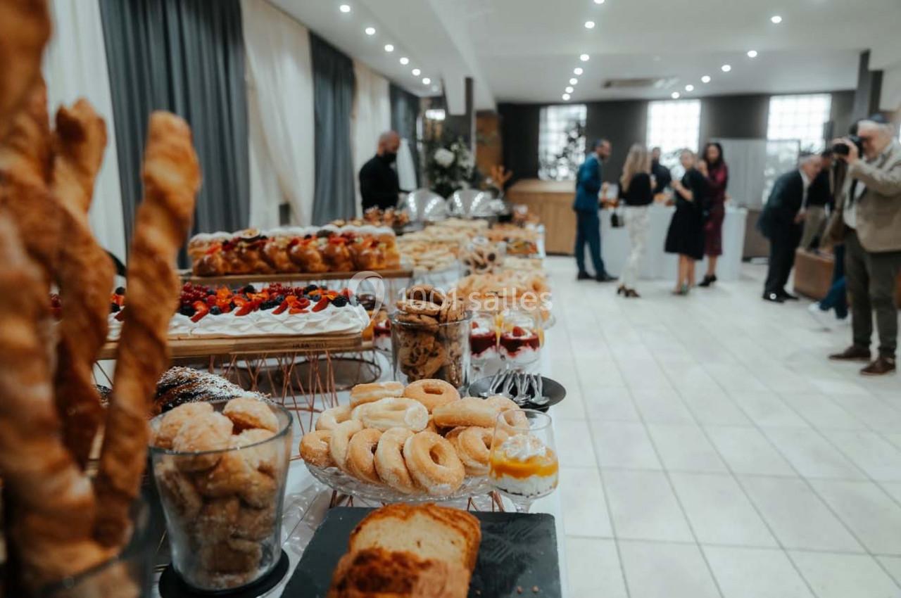 Buffet de pâtisseries variées disposées sur des tables dans une salle lumineuse avec des invités en arrière-plan.
