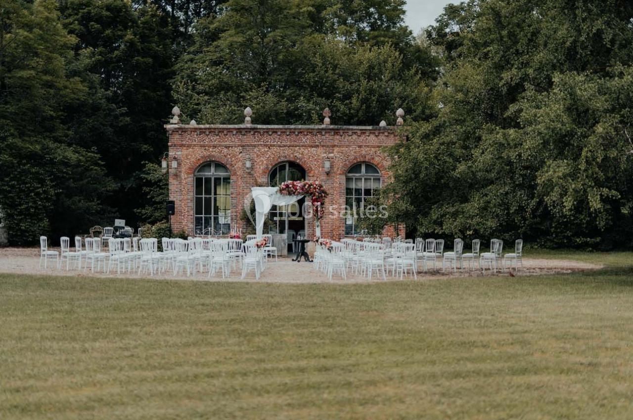 Chaises blanches disposées en extérieur devant un bâtiment en briques, décoré pour une cérémonie.