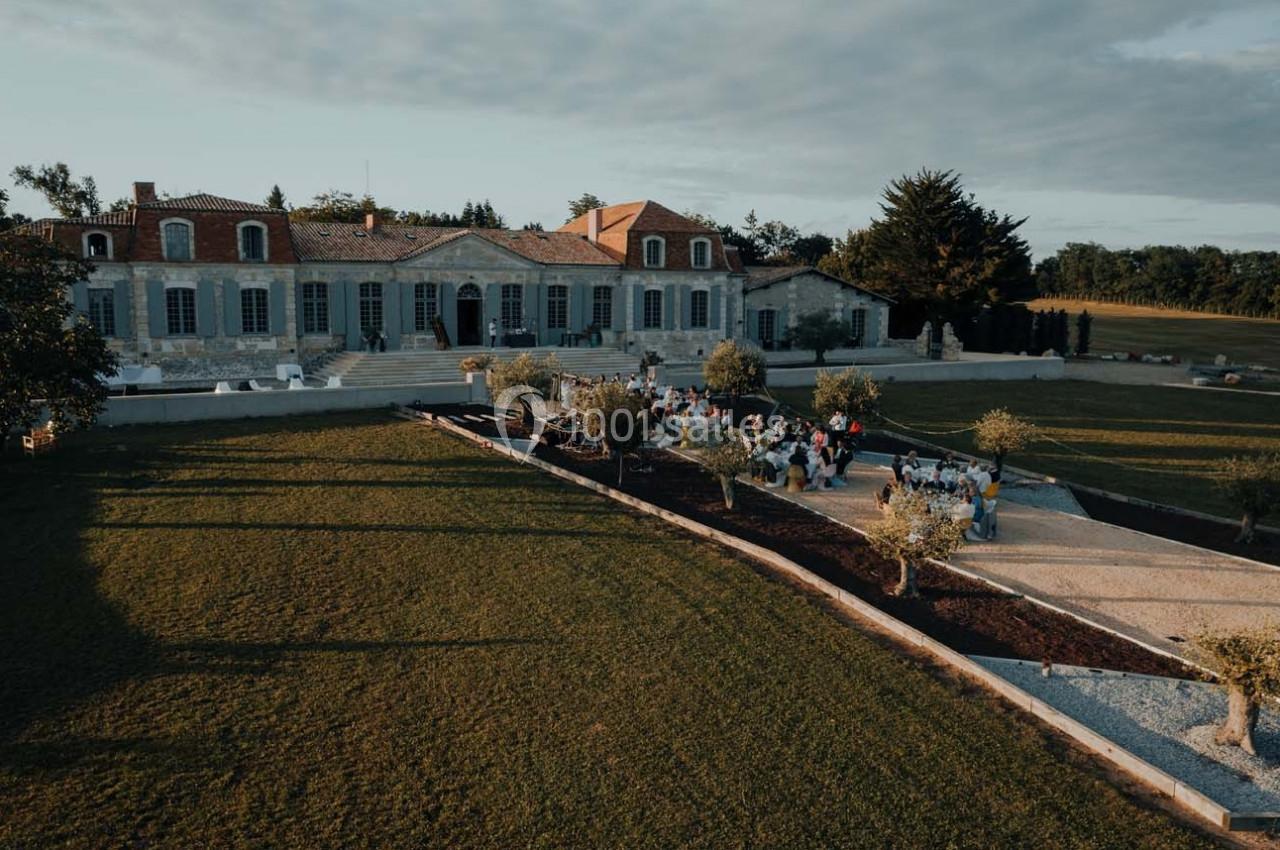 Vue aérienne d'un domaine avec une grande bâtisse en pierre, des jardins aménagés et un groupe de personnes réunies.