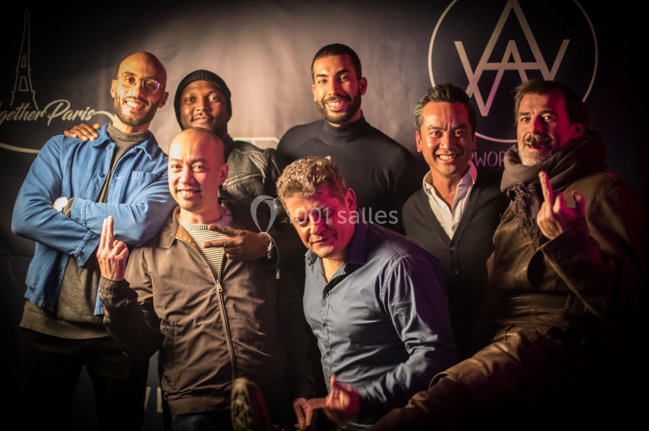 Un groupe de sept hommes posant ensemble devant un fond sombre avec des logos visibles en arrière-plan.