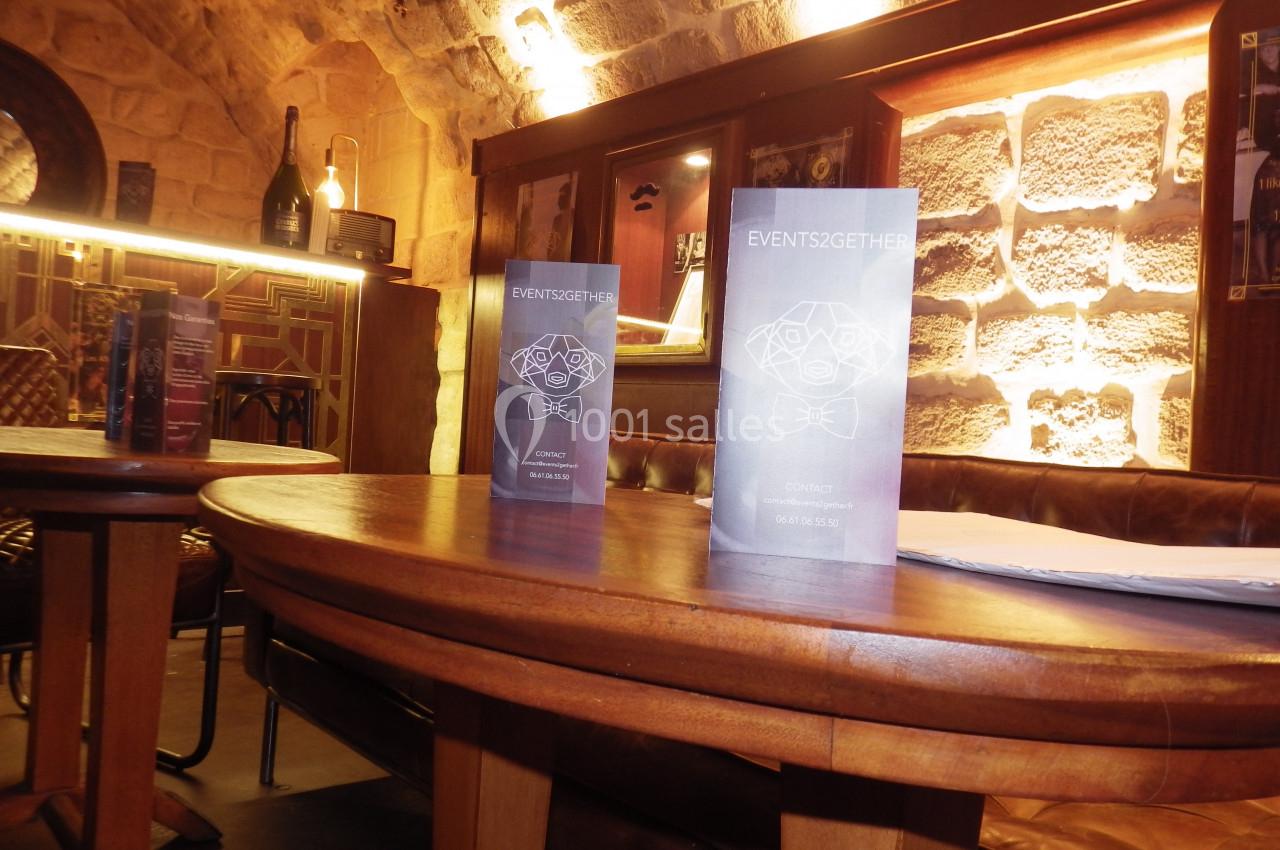 Menus posés sur une table ronde en bois dans un intérieur chaleureux avec murs en pierre et éclairage tamisé.