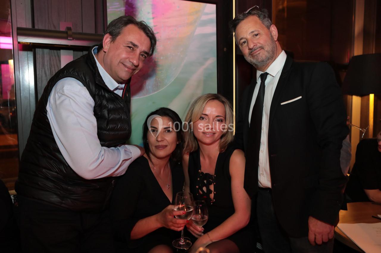 Quatre personnes posent ensemble dans un environnement intérieur chaleureux, deux assises tenant des verres.