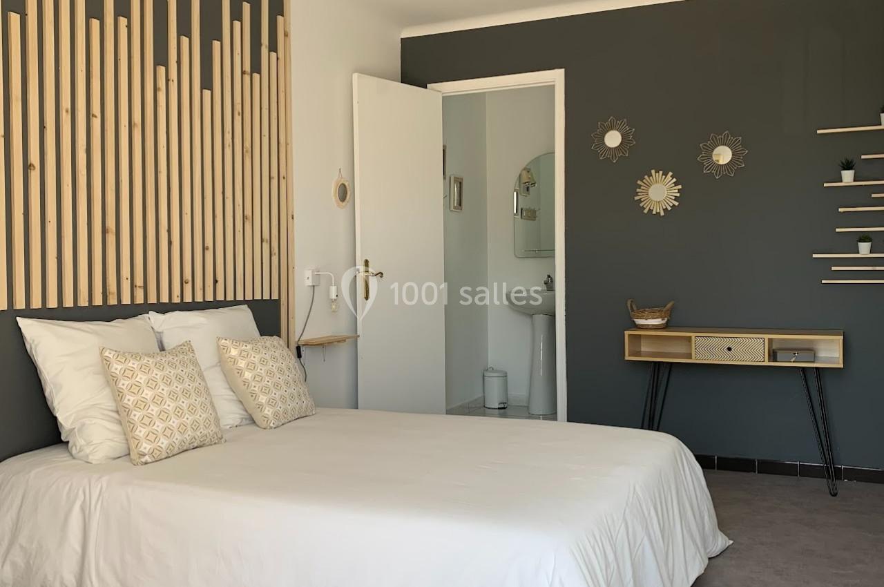 Chambre lumineuse avec lit double, décoration murale en bois et accès à une salle de bain attenante.