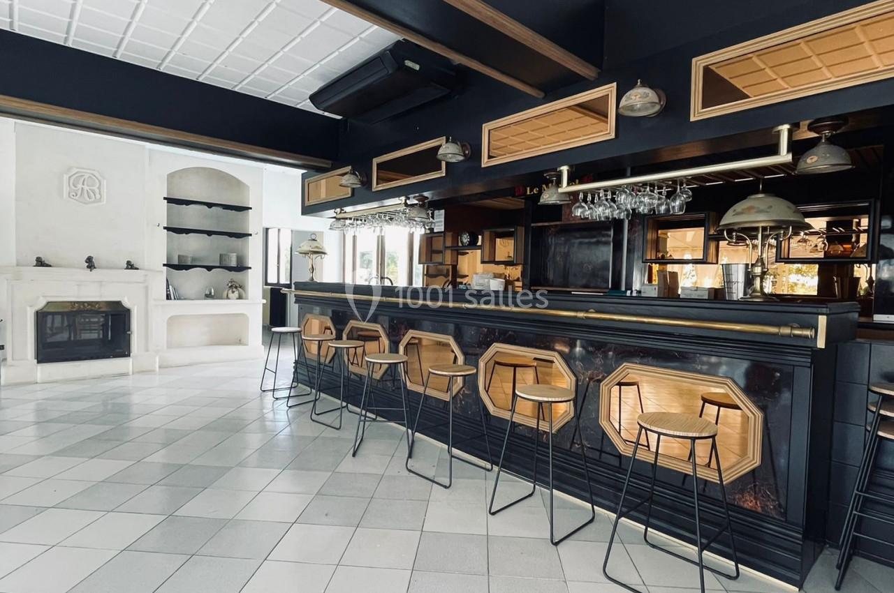 Intérieur d'un bar moderne avec comptoir en bois, tabourets hauts, étagères et cheminée en arrière-plan.