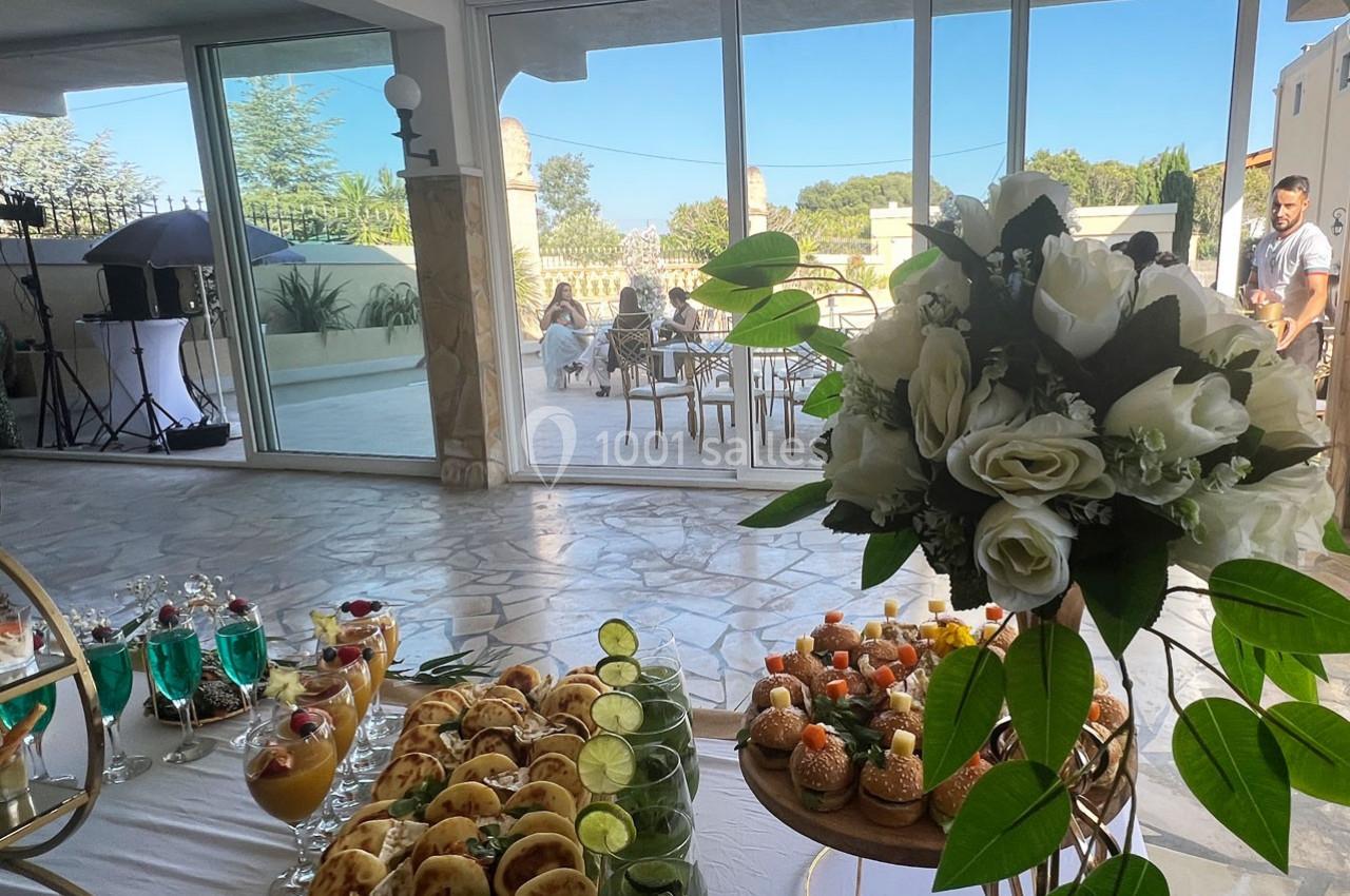 Buffet de desserts et boissons colorées en intérieur, avec vue sur une terrasse ensoleillée et des invités à l'extérieur.