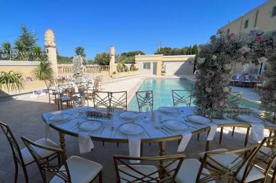 Miniature Location salle Lambesc (Bouches-du-Rhône) - Villa Maya Provence #3 Salle lumineuse avec tables rectangulaires, chaises noires et verrerie suspendue, donnant sur de grandes fenêtres.