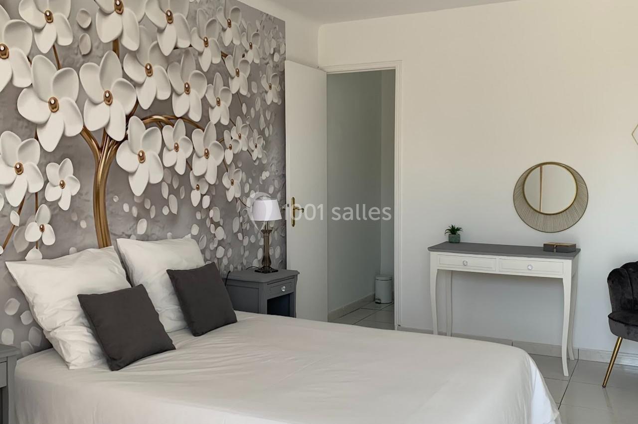Chambre lumineuse avec lit double, mur décoré de fleurs en relief, bureau blanc et miroir rond.