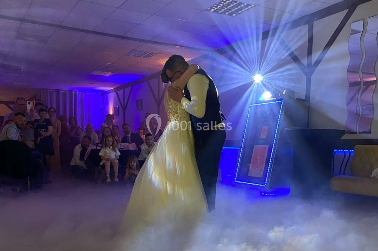 Un couple danse enlacé sous des lumières tamisées, entouré de spectateurs dans une salle décorée.