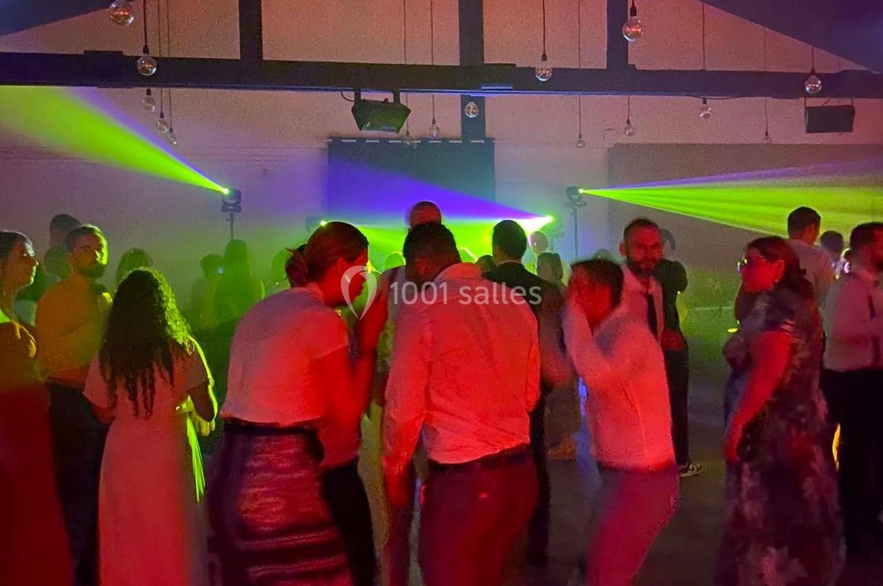 Des personnes dansent dans une salle sombre éclairée par des lumières colorées et des faisceaux lumineux.