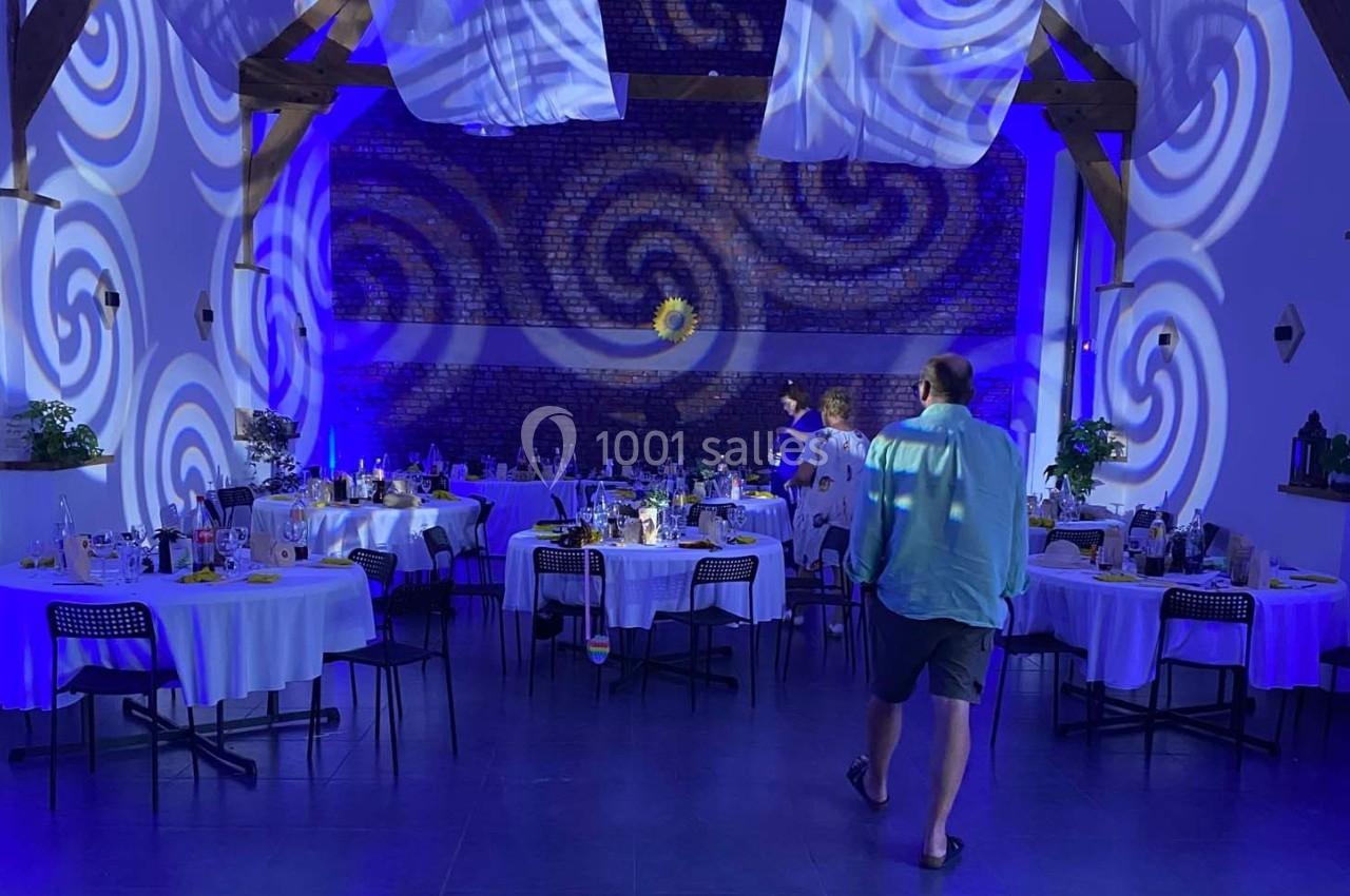 Salle de réception décorée avec des tables rondes dressées, éclairage bleu et motifs lumineux projetés sur les murs.