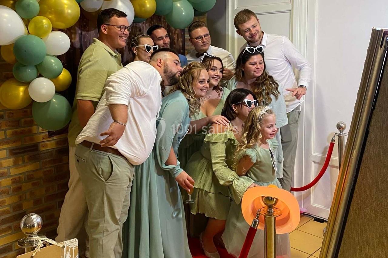 Un groupe de personnes pose devant un photobooth, entouré de ballons décoratifs et d'une corde rouge.