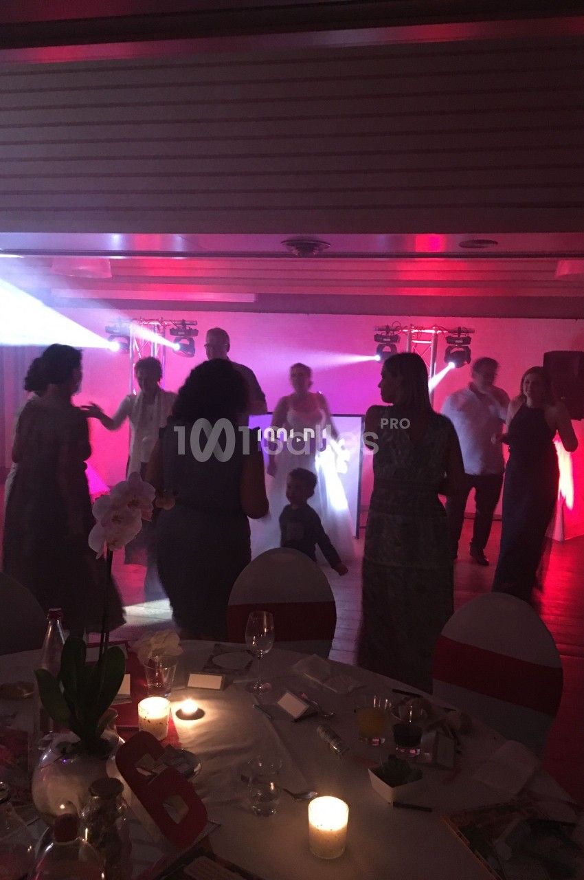 Des personnes dansent dans une salle faiblement éclairée avec des lumières colorées et une table dressée au premier plan.