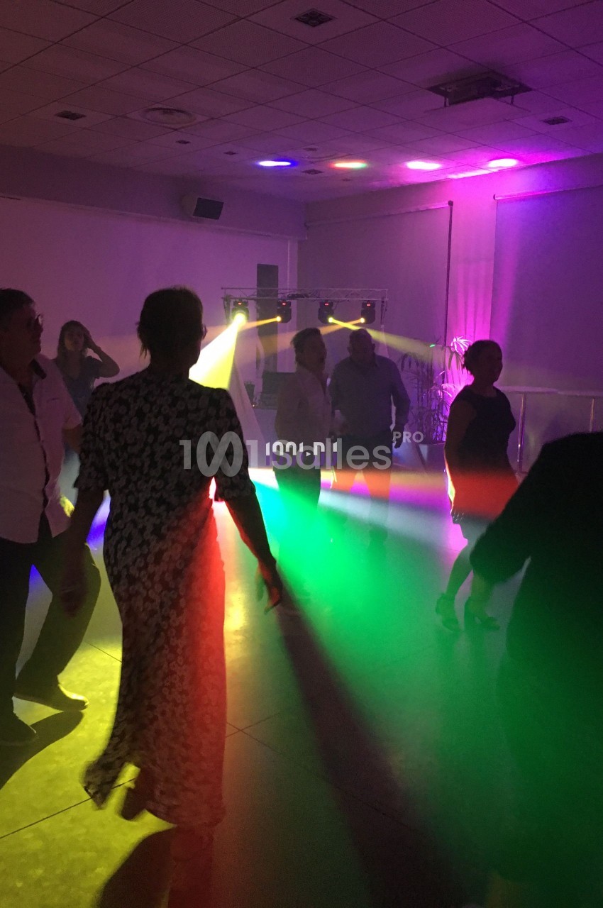 Des personnes dansent dans une salle sombre éclairée par des lumières colorées et des projecteurs.