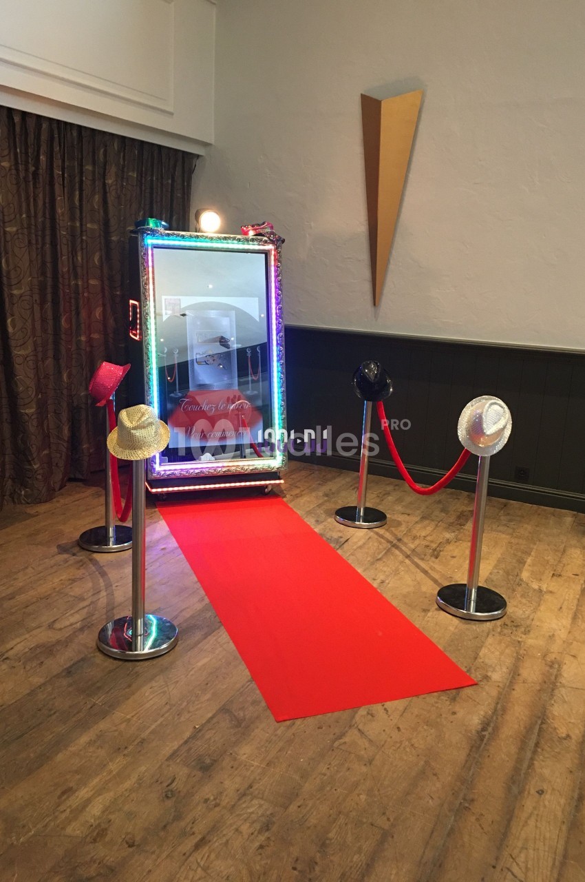 Miroir interactif lumineux avec accessoires et tapis rouge, installé dans une salle au sol en bois.