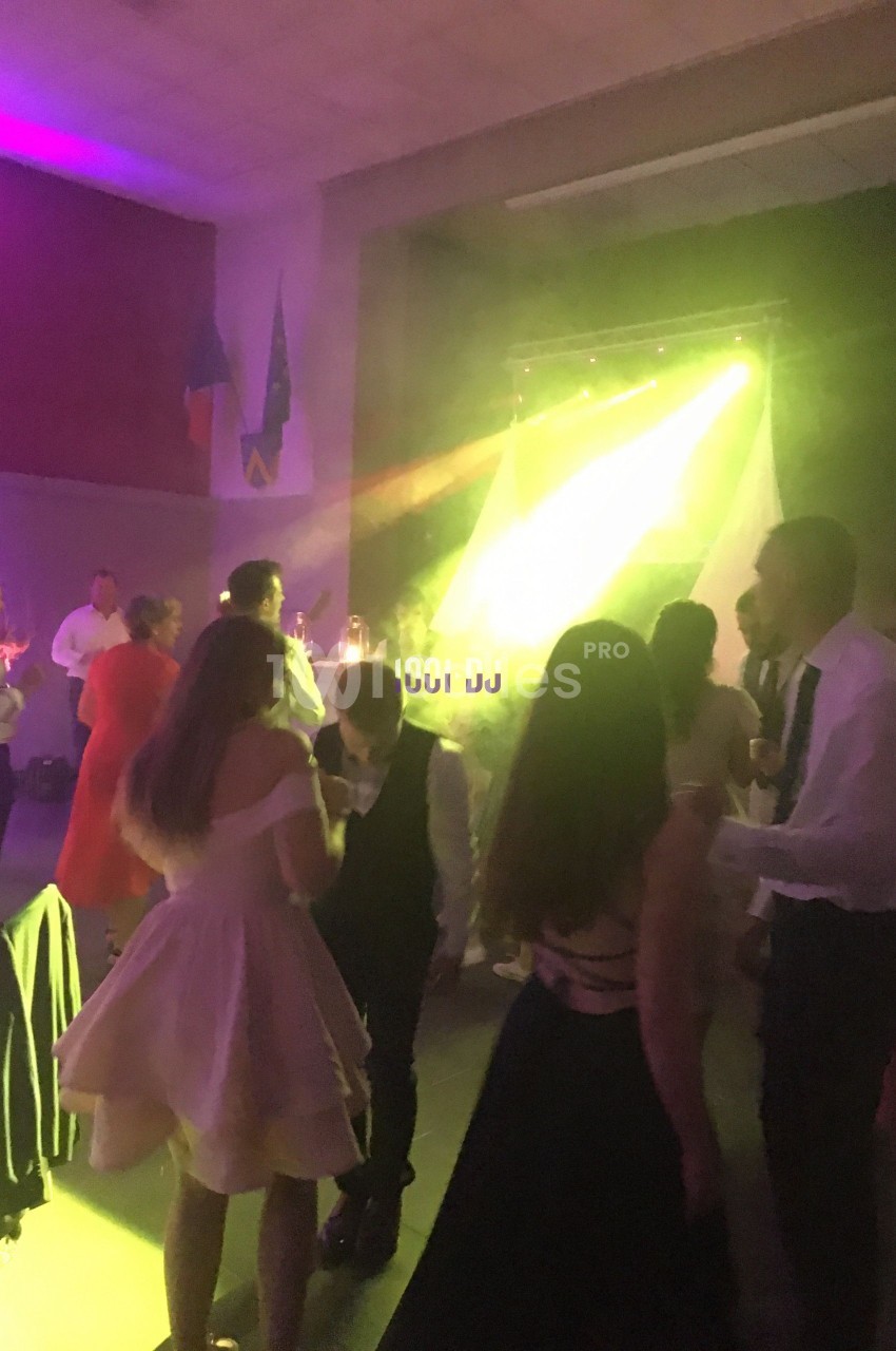 Des personnes dansent dans une salle éclairée par des lumières colorées, avec un DJ en arrière-plan.