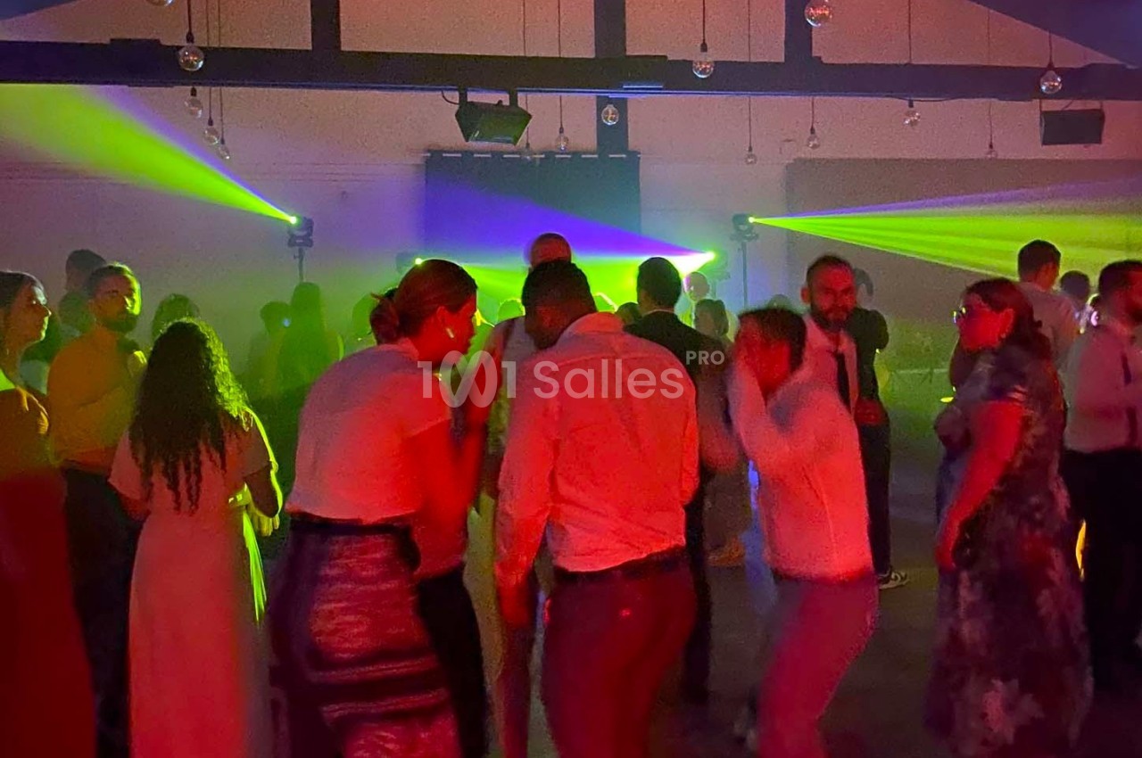 Des personnes dansent dans une salle sombre éclairée par des faisceaux lumineux colorés.