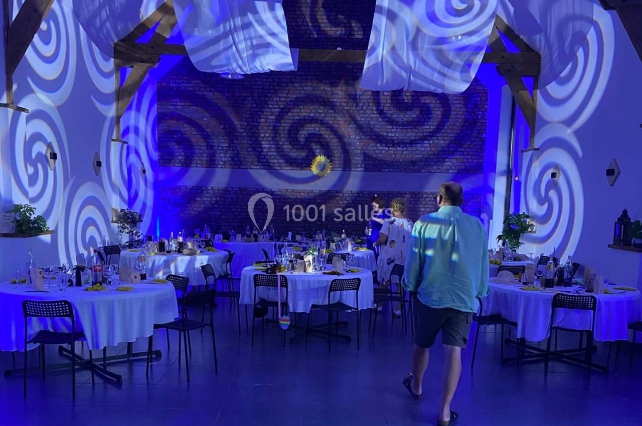 Salle de réception décorée avec des nappes blanches, éclairages bleus et motifs tourbillonnants projetés sur les murs.