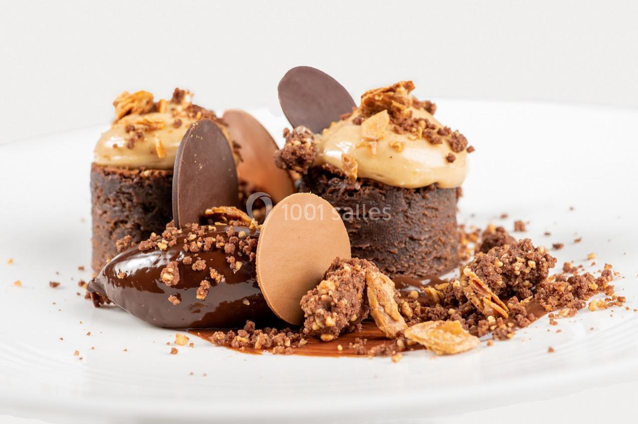 Dessert composé de petits gâteaux au chocolat, mousse, éclats croustillants et disques de chocolat sur une assiette blanche.