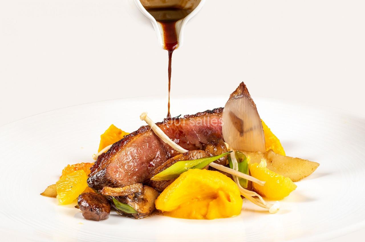 Tranche de viande cuite servie avec légumes colorés et sauce versée sur une assiette blanche.
