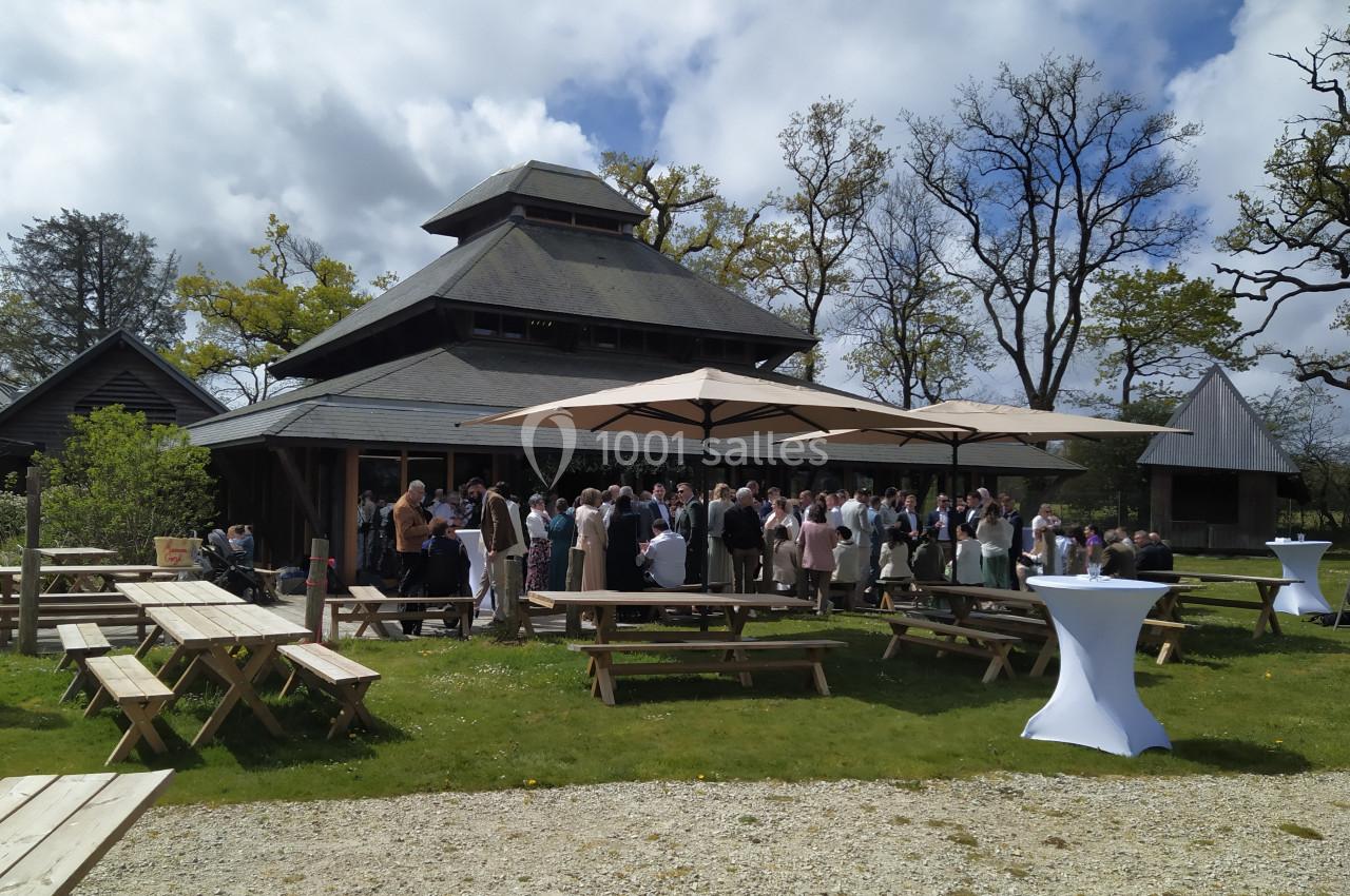 Groupe de personnes rassemblées devant un bâtiment en bois avec des tables de pique-nique et des parasols dans un jardin.
