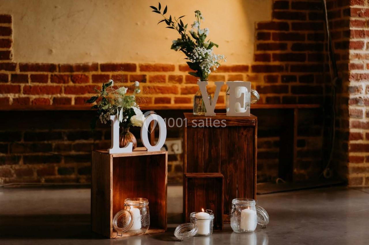 Décoration composée de caisses en bois, bougies et fleurs, avec les lettres formant le mot ’LOVE’ sur fond de mur en briques.