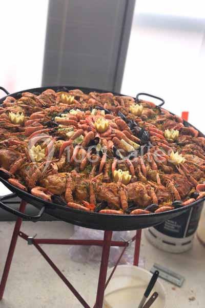 Grande poêle de paella garnie de fruits de mer, poulet, moules et décorations en citron, posée sur un trépied.