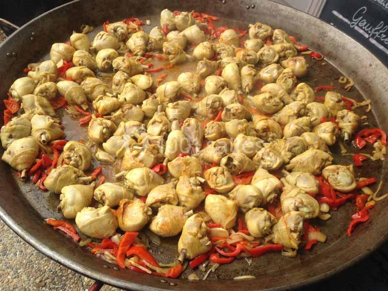 Morceaux de poulet cuits dans une grande poêle avec des lamelles de poivrons rouges et des oignons.