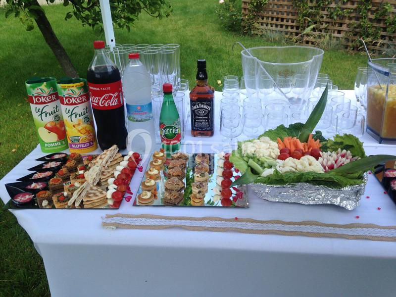 Buffet en extérieur avec boissons, verrines, toasts variés et plateau de crudités sur une table blanche.