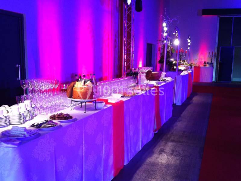 Buffet élégant avec nappes blanches, verres, plats variés et éclairage coloré dans une salle événementielle.