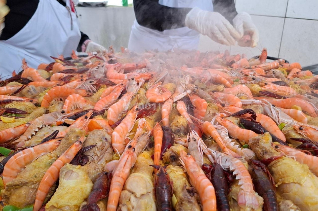 Gros plan sur une grande paella garnie de crevettes, langoustines, morceaux de poulet et légumes, en cours de préparation.