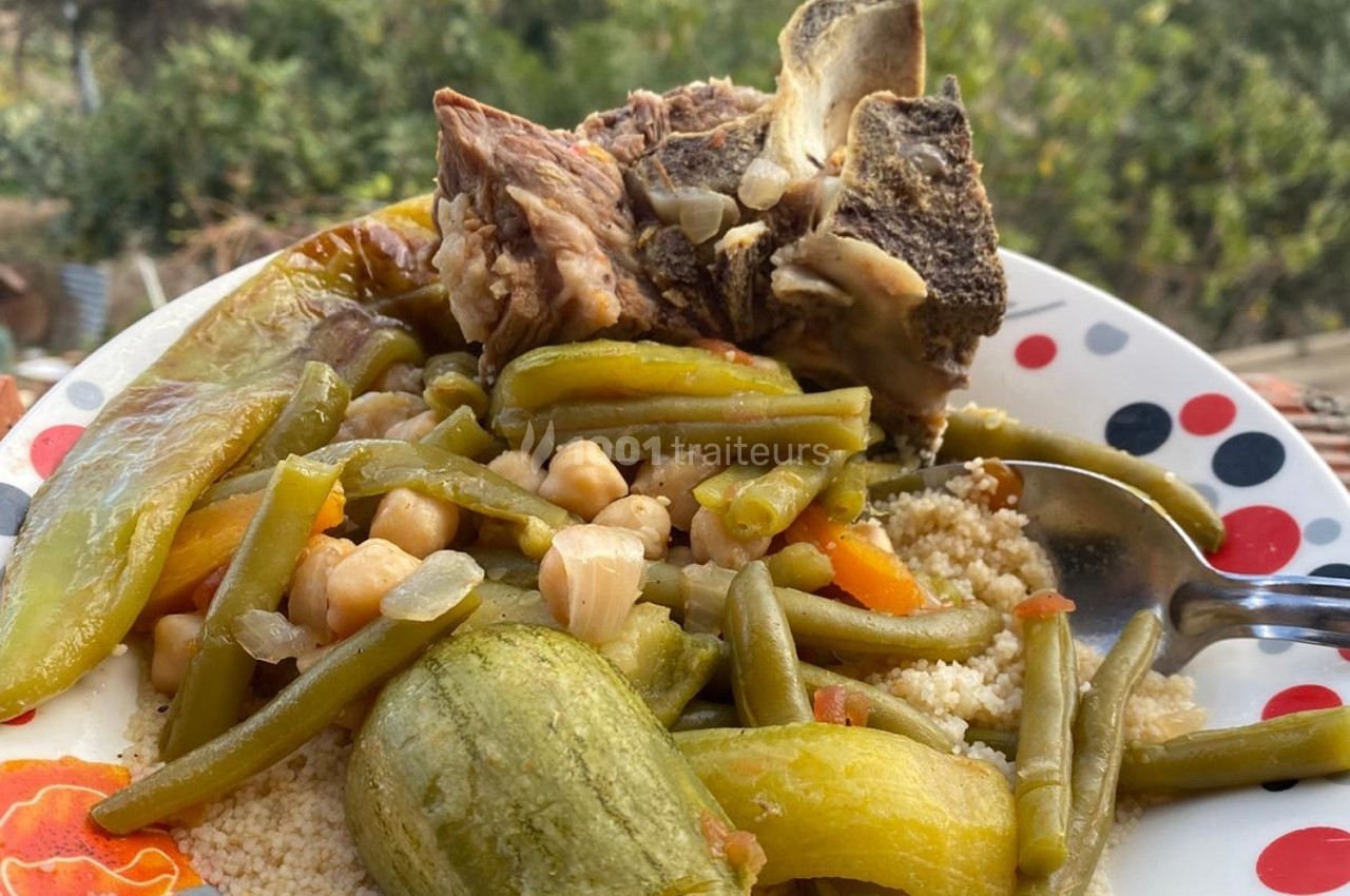 Assiette de couscous avec légumes variés, pois chiches et morceaux de viande, servie en extérieur.