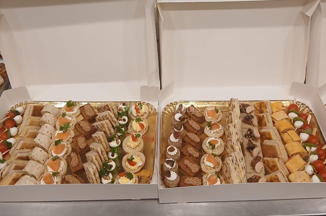 Plateaux garnis de divers amuse-bouches, incluant toasts, roulés, œufs mimosa et bouchées salées, présentés dans des boîtes…