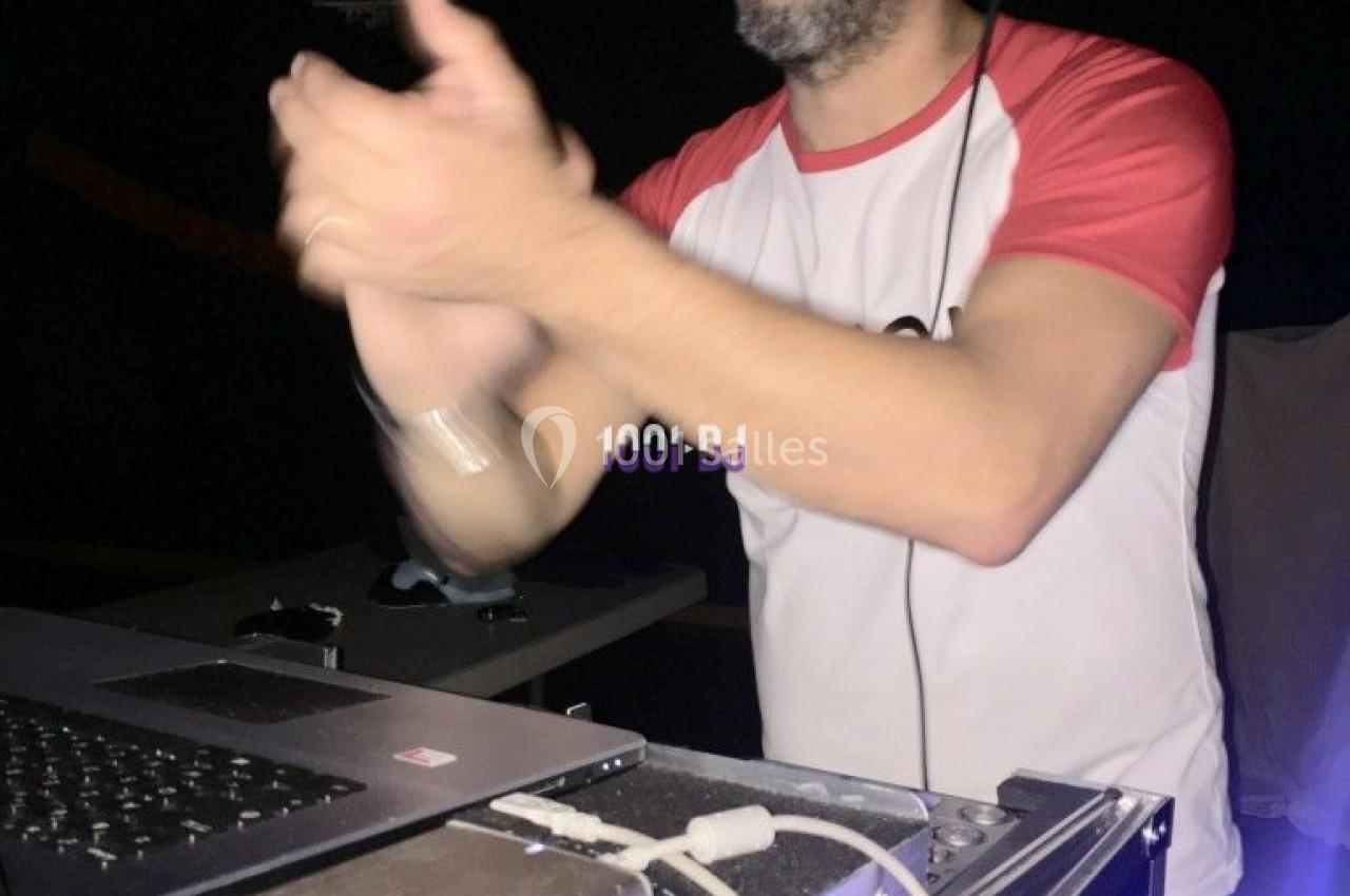 Un homme en t-shirt et casquette utilise un équipement de DJ avec un ordinateur portable dans un environnement sombre.