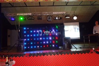 Un DJ mixe derrière une table éclairée de lumières LED violettes, avec un mur décoratif en arrière-plan.