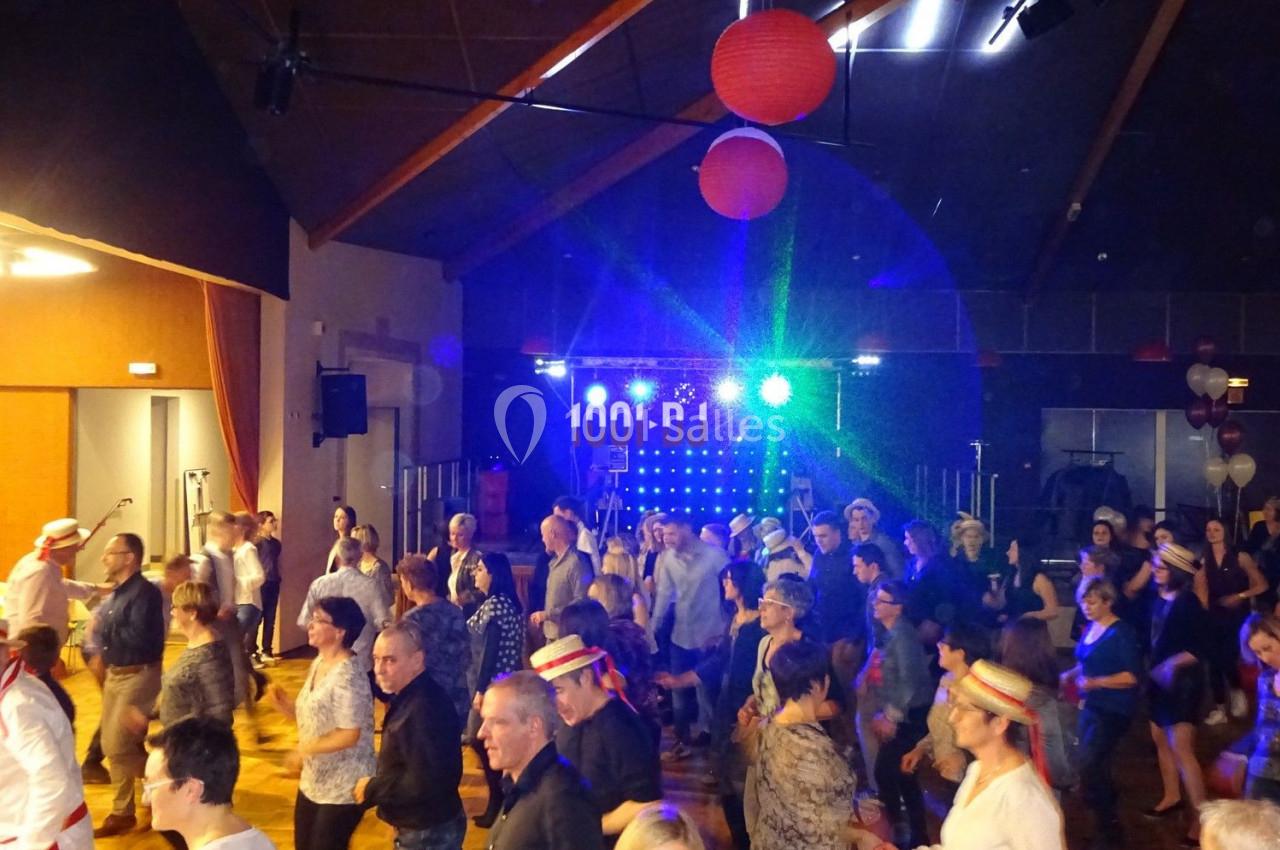 Groupe de personnes dansant dans une salle éclairée par des lumières colorées, avec une scène en arrière-plan.
