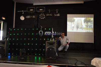 Un DJ mixe derrière une table éclairée de lumières LED violettes, avec un mur décoratif en arrière-plan.