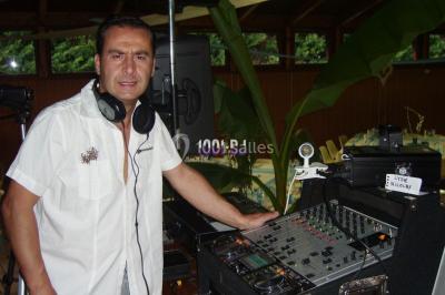 Un DJ mixe derrière une table éclairée de lumières LED violettes, avec un mur décoratif en arrière-plan.